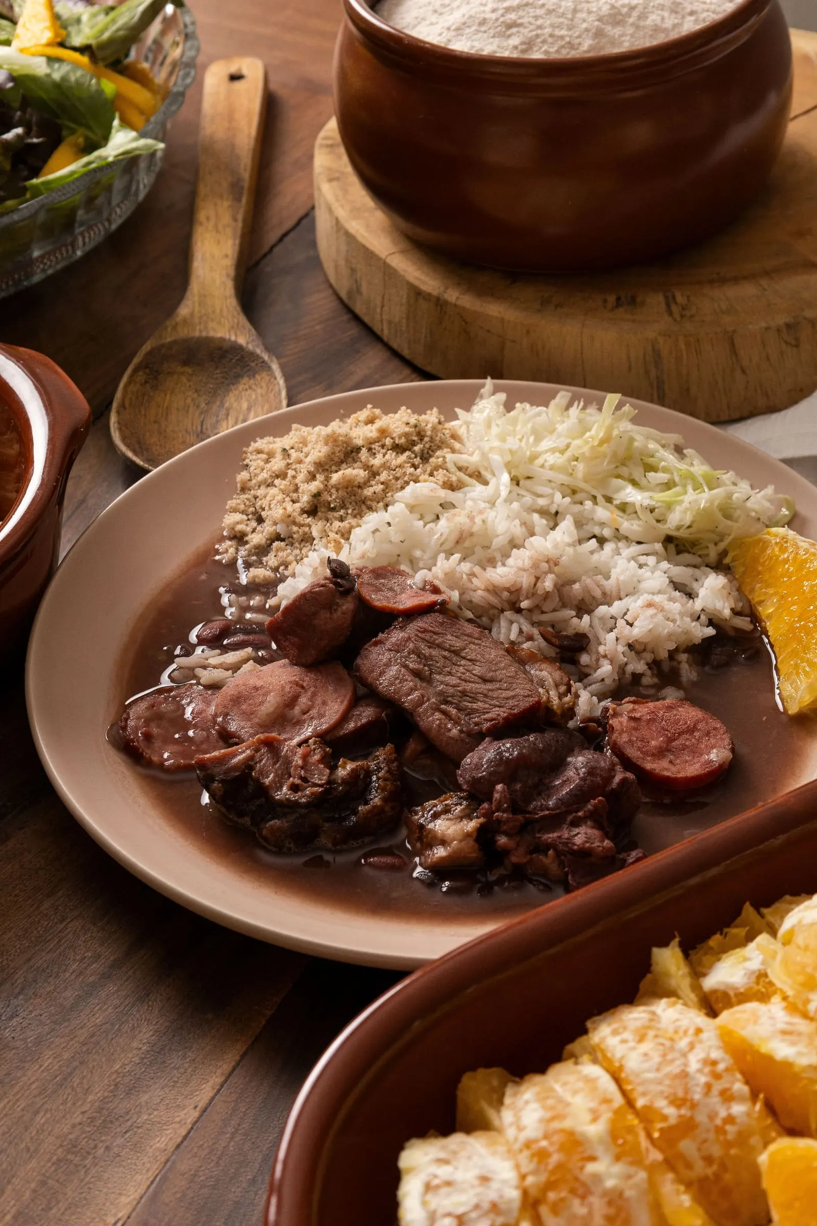 A plate of feijoada with rice, farofa, orange, and collard greens